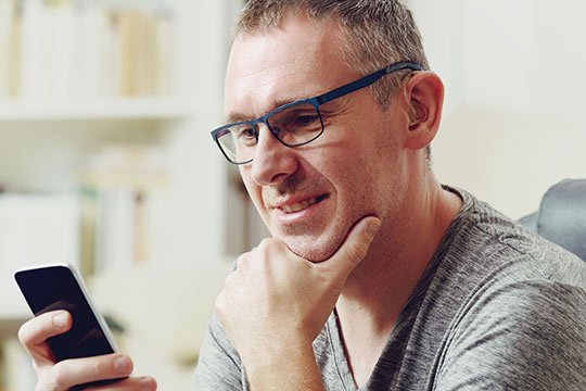 Man smiling while using smartphone with hearing aids